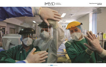 Three women wearing the medical protective suit against COVID-19 put their hands on a glass window to join hands on the other side